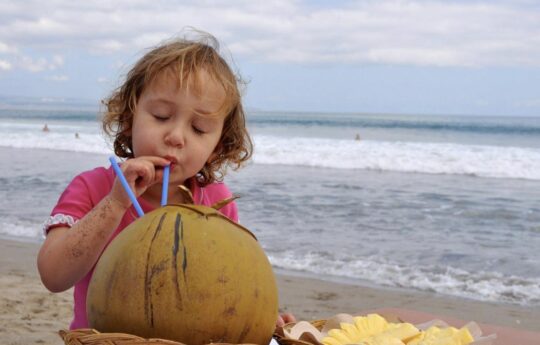 Tips_for_Surviving_a_Bali_Holiday_with_a_Toddler Child having a coconut on the beach in bali