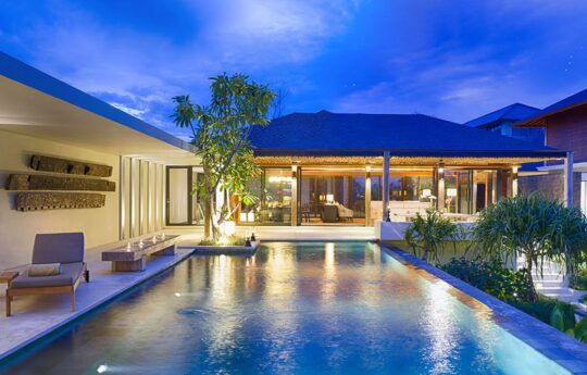Swimming pool at night with lights reflecting on pool and villa exterior