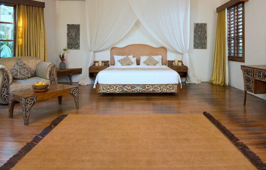 Bedroom of villa with king bed and large rug with day chair
