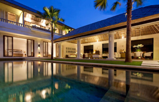 Two level villa exterior at night with lights on and shimmering swimming pool