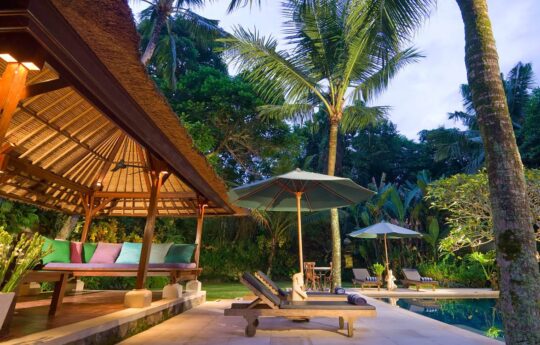 Outdoor gazebo area next to pool with day beds at dusk