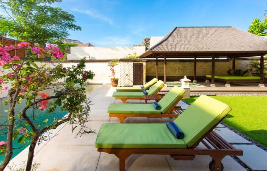 Day beds by swimming pool at villa with grassy area