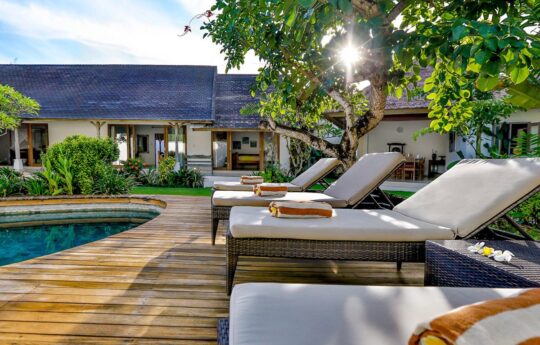 Day beds by swimming pool with villa exterior during day