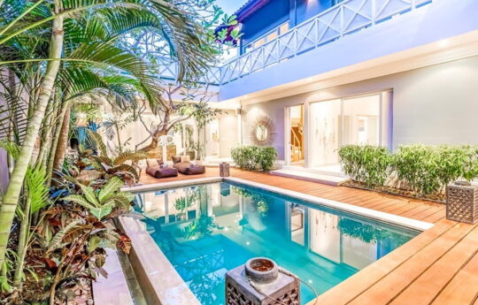 Vlla Moana Swimming pool, deck area with plants in foreground and villa exterior at night with lights on