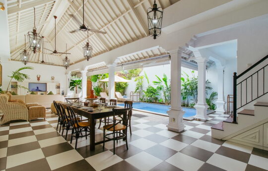 Open plan tropical living areas of villa with swimming pool in background