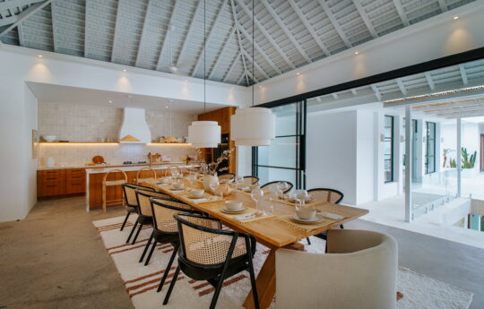 Dining table for eight people with kitchen in background of villa