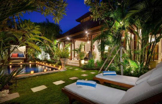 Swimming pool and day beds of villa at night with villa exterior lights on