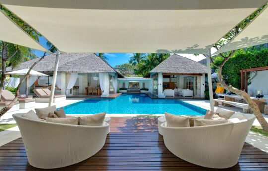 View of villas swimming pool on sunny day from gazebo area with sun deck chairs