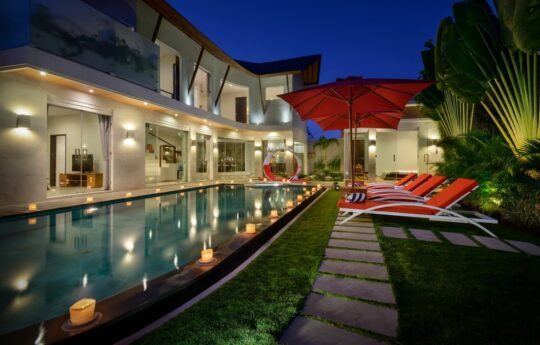Swimming pool at night with lights on and villa exterior