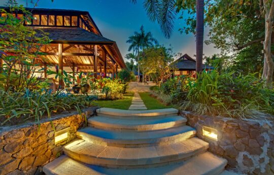 Villa exterior at dusk with lights on and garden views