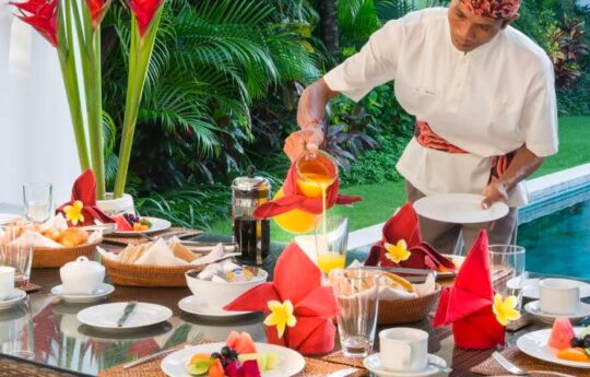 staff of seminyak villa serving breakfast with swimming pool in background