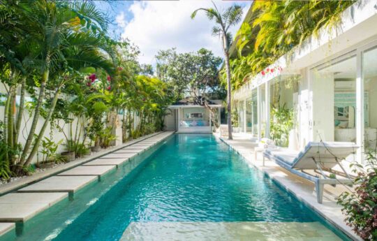 Swimming pool on sunny day with lush gardens and villa exterior