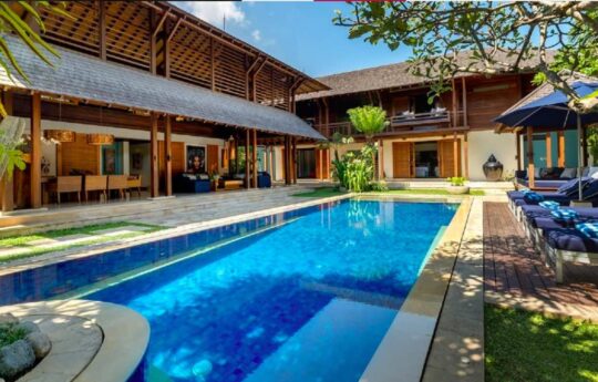 Swimming pool on sunny day with two level villa exterior in background
