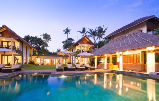 Exterior of villa t night with lights on and swimming pool