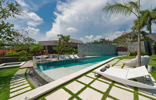 Swimming pool of villa with day beds on sunny day and villa exterior glimpses