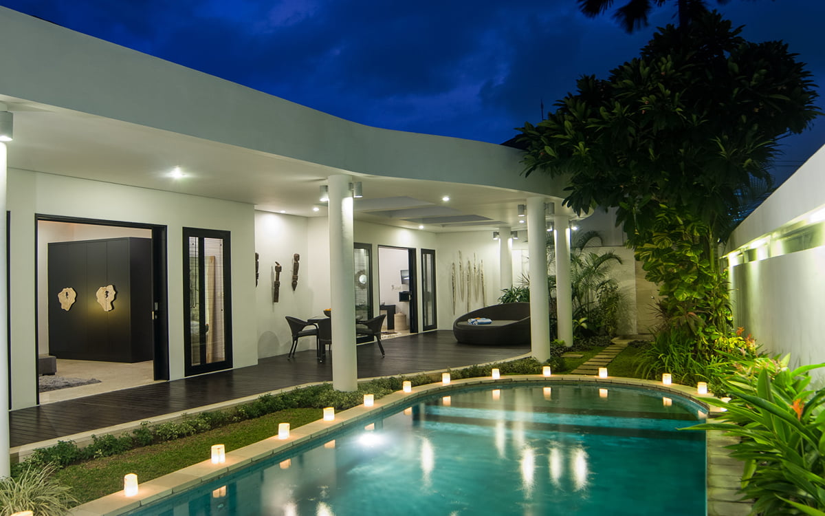 Swimming pool and villa exterior at night with lights on at dusk