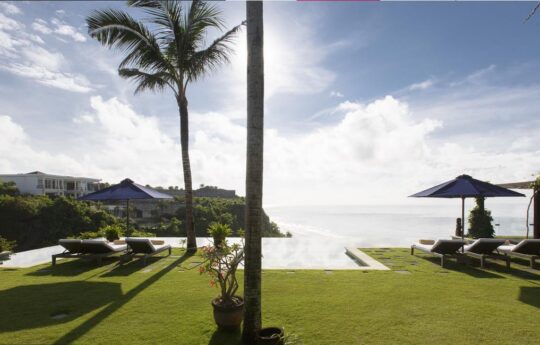clifftop views of ocean with pool and day beds under blue bali skies