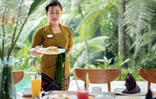 balinese staff of villa serving breakfast with garden views in background