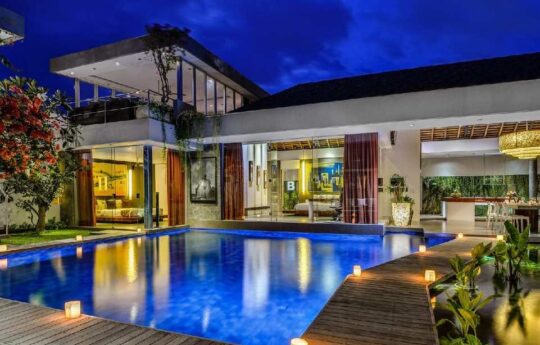 Swimming pool at night with view of Villa Banyu exteriors in background with lights on