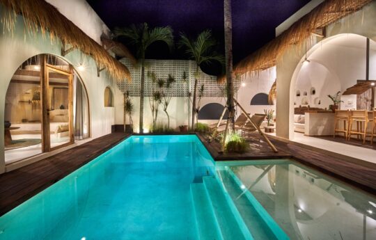 Swimming pool at night with lights on and view of bedrooms and villa main living areas