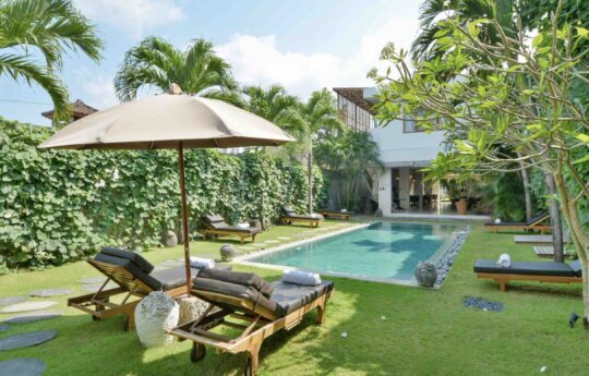 Two day beds by pool with grassy garden area with villa in background