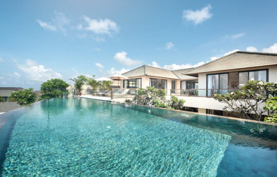 Close up of swimming pool with villa exterior in background on sunny day