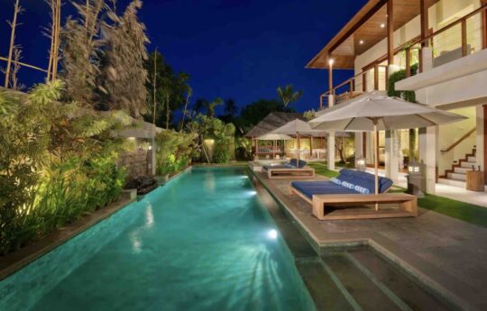 Swimming pool views with two level villa in background at night with lights on