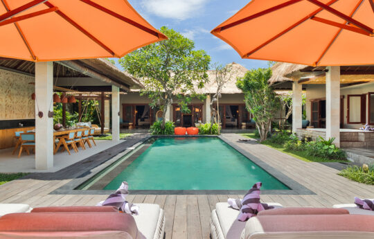 Large swimming pool with 2 days beds with umbrellas in foreground