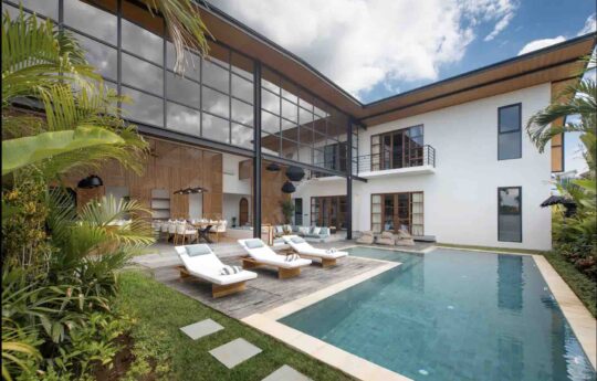 Swimming pool of villa during daytime with two storey modern villa exterior and day beds