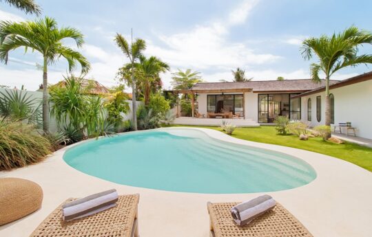 Villa Panas Sekali Pool area with day beds of Villa Panas Sekali with palm tres and villa exterior in background