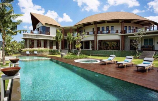 Swimming pool with sun deck and three day beds with villa exterior in background