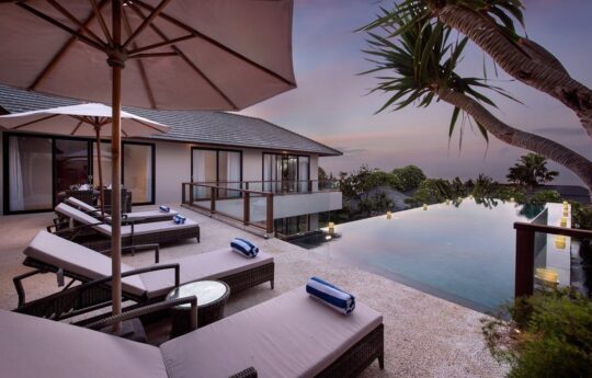 Swimming pool with deck chairs at sunset with distant ocean glimpses