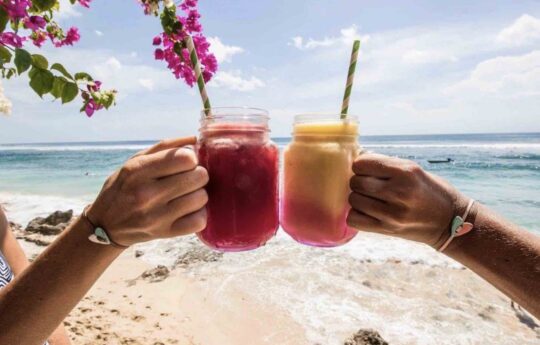 two people holding tropical fruit juice on sunny beach